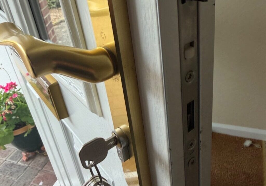 View of white front door partially open with a gold handle, euro cylinder lock with keys inserted and part of the door frame visible, inside a home on Manston Drive, Bishop's Stortford.