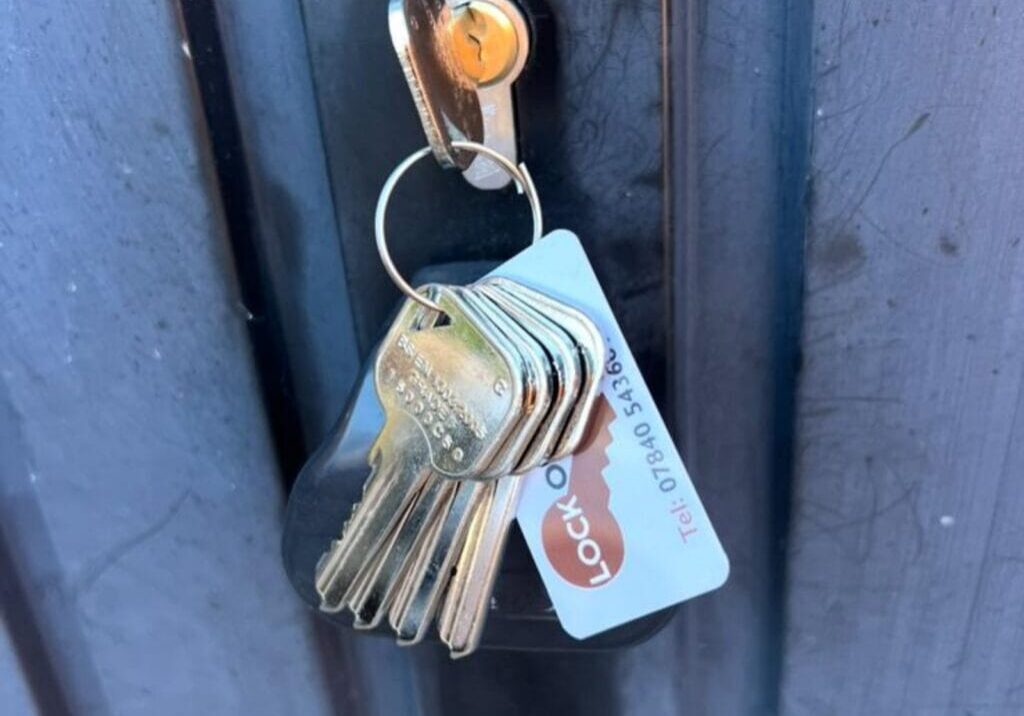 Close-up of a newly installed lock cylinder on a black garage door with five keys on a keyring inserted in the lock