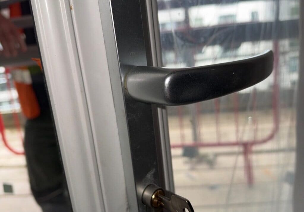 Close-up of the handle and euro profile cylinder lock on a UPVC French door with a key inserted and a keyring attached. The background shows scaffolding outside.