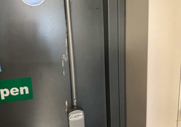 Gray commercial fire door on Enterprise Drive in Braintree showing a push bar and a round deadlock thumbturn