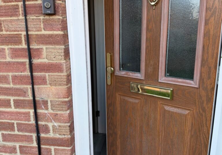 Close-up view of a partially open wooden front door with glass panels and a brass letterbox and door knocker, set in a brick wall on Dukes Road, Braintree