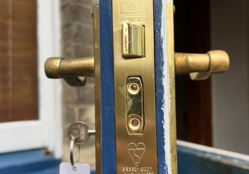 Close-up of a brass rim cylinder lock installed on a blue front door with a key inserted