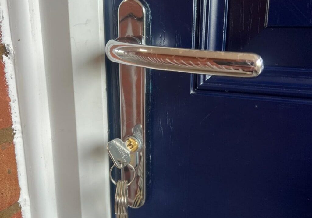 Close-up of a newly fitted silver lock on a blue composite front door with a set of five keys in the lock
