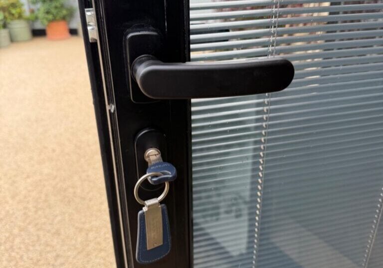 Close-up view of a black bi-fold door handle on a glass door with a key inserted in the lock, from a slightly different angle in Great Dunmow