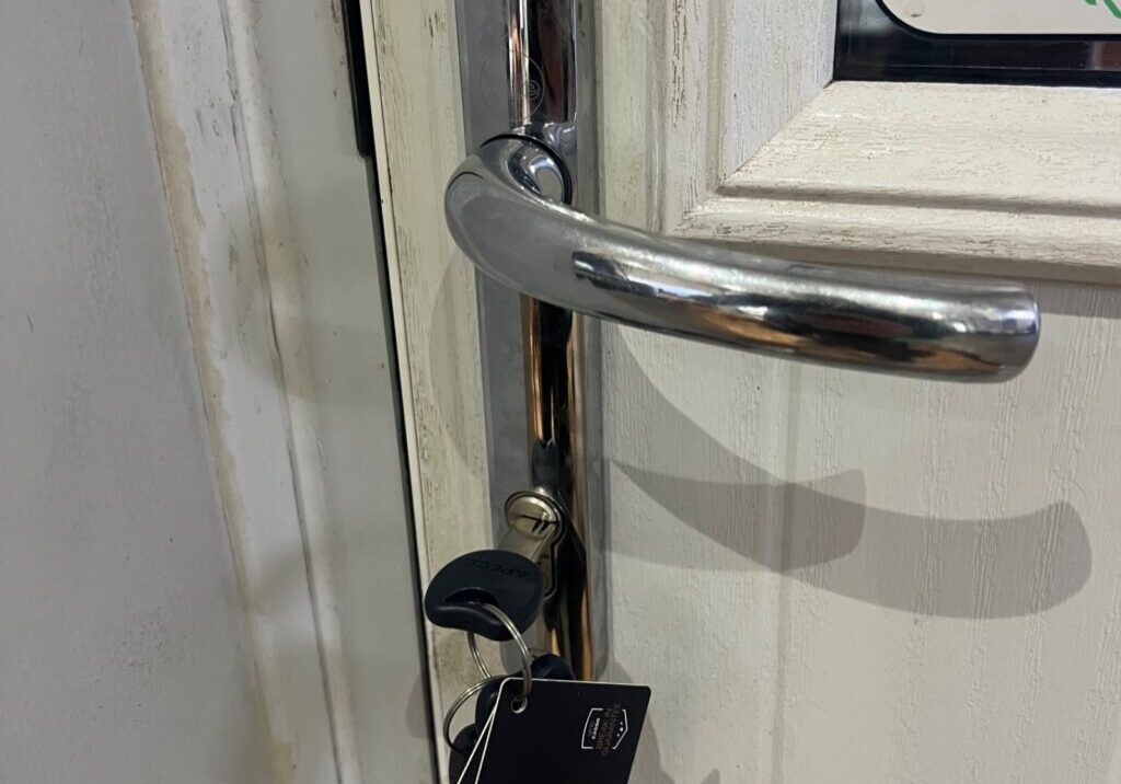 Close-up of a keyed-alike three-star high-security lock cylinder with an APECs key inserted in a white door in Great Notley.