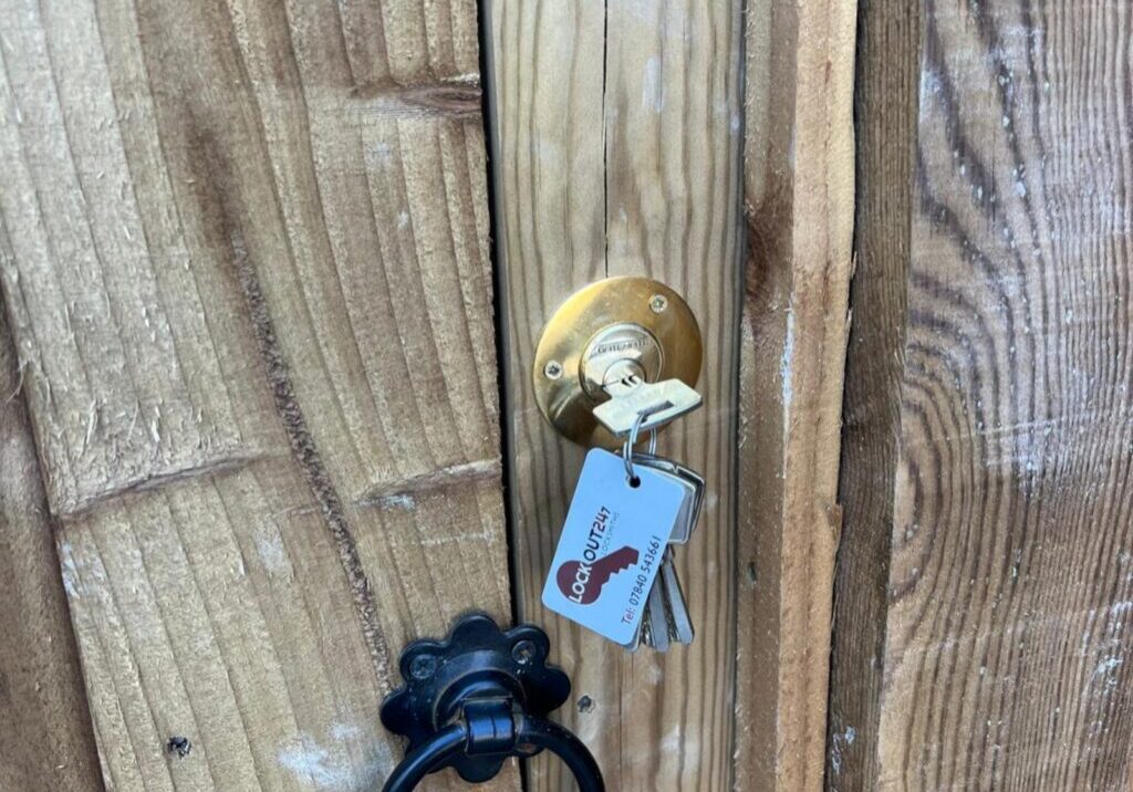 Close-up photograph showing a brass lock with a key inserted, fitted on a wooden garden gate.