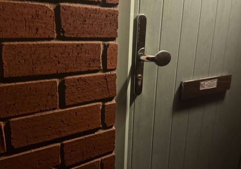 Close-up view of a green uPVC front door with a round window, handle, and letterbox, set in a brick wall in Wallis Court, Stanway.