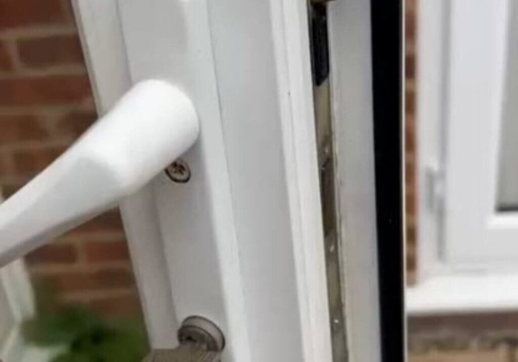 Close-up view of a white UPVC door handle with a key inserted in the lock cylinder showing part of the door frame and brick wall in Wethersfield