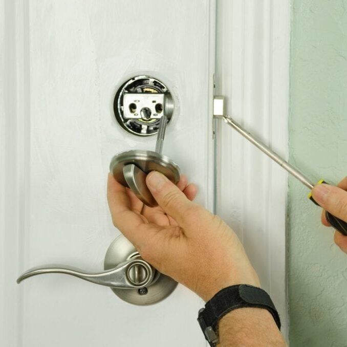 Closeup of a professional locksmith is installing or repairing a new deadbolt lock on a house exterior door with the inside internal parts of the lock visible.